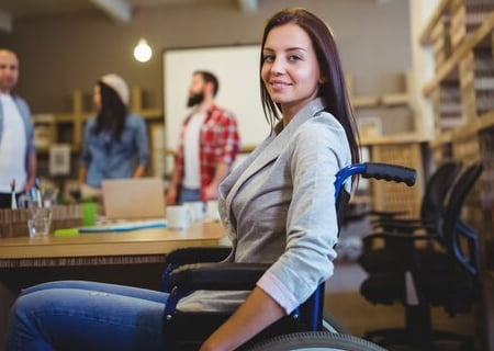 Una joven en silla de ruedas, vestida elegantemente, en una mesa de reuniones con otros compañeros de trabajo