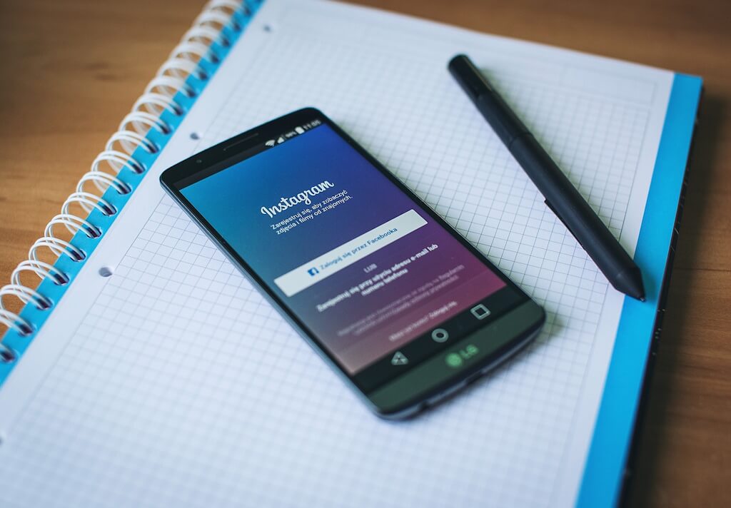 Sobre una libreta de anillas con papel cuadriculado y bordes azules, vemos un móvil que muestra la aplicación Instagram junto a un lápiz digital