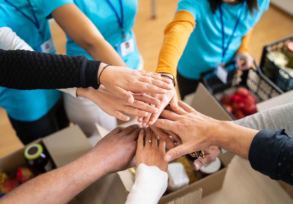 Varias personas, de diferentes etnias edades, unen las manos sobre cajas con comida